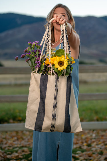 Woman holding a striped tote bag with flowers against a mountainous background